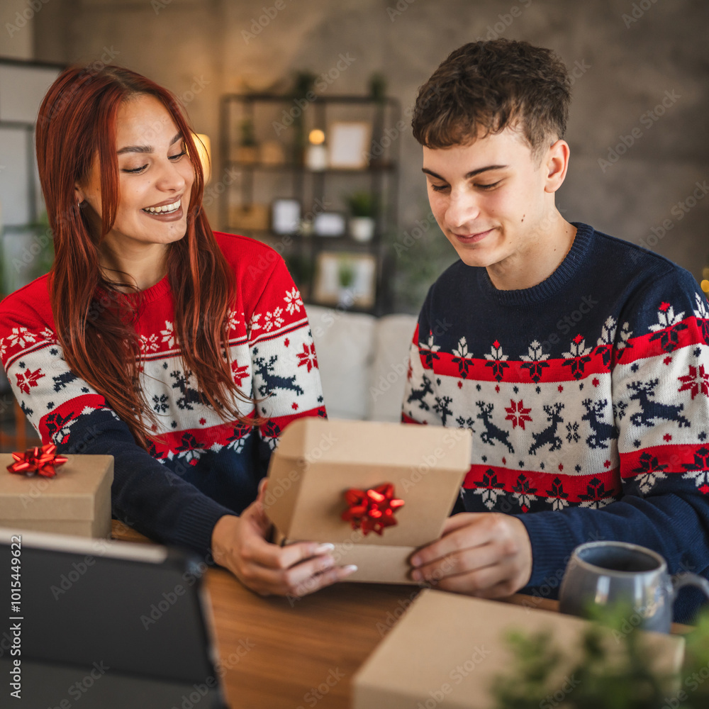 Wall mural young couple wrap gift during video call, holiday spirit shines bright