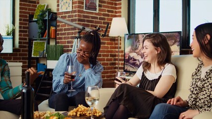 Culturally inclusive group of women talking, drinking wine at reunion gathering, gossiping about their boyfriends. Asian, african american and caucasian girls enjoying social life in living room