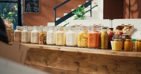 Various bulk items in reusable jars at zero waste eco store, selling nonpolluting homemade cooking supplies and produce. Small business in farming advertising healthy eating. Handheld shot.