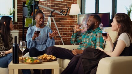 African american woman telling story while friends enjoys tasty treats in brick wall living room, talking and sharing funny stories at apartment party, having brunch together, consuming snacks