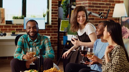 Portrait of african american man talking with friends in stylish apartment living room, gathered together to celebrate festive event. Diverse group of people socializing at home, enjoying appetizers
