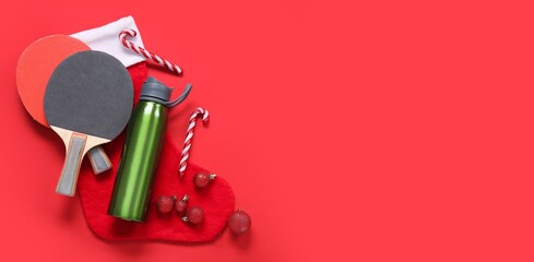Composition with sports bottle, ping pong rackets and Christmas decorations on red background with space for text