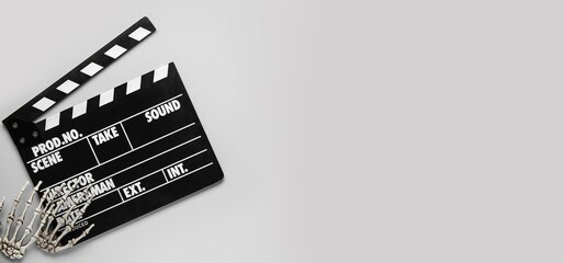 Naklejka premium Clapperboard with skeleton hands on grey background with space for text