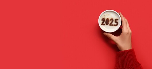 Female hand and cup of hot coffee with figure 2025 on red background with space for text