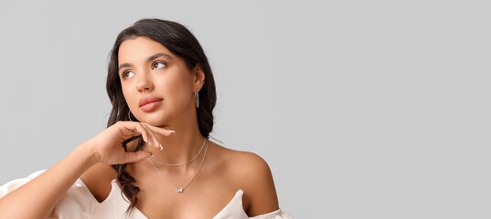 Stylish young woman with beautiful jewelry on grey background with space for text