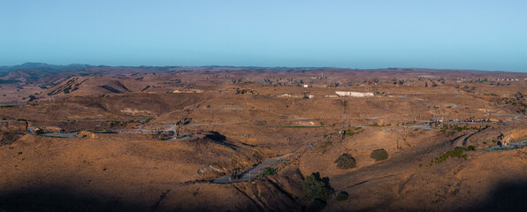 The image shows a vast desert landscape with oil rigs, rolling hills, and sparse vegetation under a...