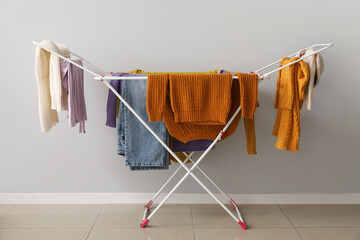 Clean winter clothes hanging on dryer near light wall