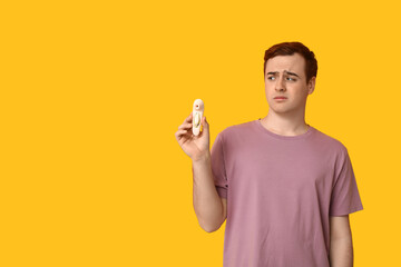 Emotional young man with vibrator on yellow background