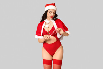 Obraz premium Beautiful young sexy woman in lingerie and Santa hat with candy cane on grey background