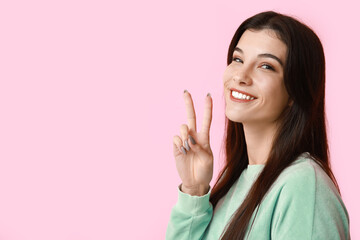 Young woman showing peace sign on pink background, closeup