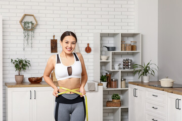 Young woman measuring her waist in kitchen. Weight loss concept