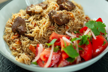 Steaming hot pilaf is served with tender lamb and a side of fresh tomato and onion salad. This hearty and flavorful dish is perfect for a satisfying meal