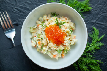 Traditional russian salad with boiled potato, carrot, dill pickle, green peas, eggs, mayonnaise and decorated with red caviar and fresh dill