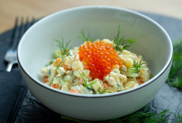 Plate of olivier salad, a traditional russian dish, is garnished with fresh dill and topped with a generous serving of bright red caviar