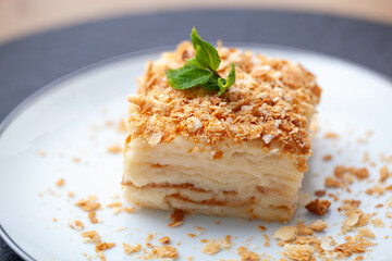 Delicious napoleon cake, garnished with a fresh mint leaf, sits on a white plate, tempting dessert lovers with its flaky layers and creamy filling