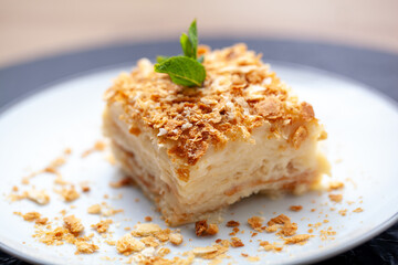 Piece of layered napoleon cake is presented on a plate, featuring flaky pastry, rich custard, and a dusting of crumbs