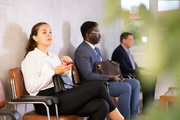 Unemployed middle age woman is waiting for conversation in hall. Several multinational candidate...