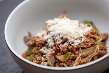 Buckwheat porridge with roasted mushrooms and onions is topped with grated cheese and dill in a white ceramic bowl. This hearty and flavorful dish is perfect for a healthy and satisfying meal
