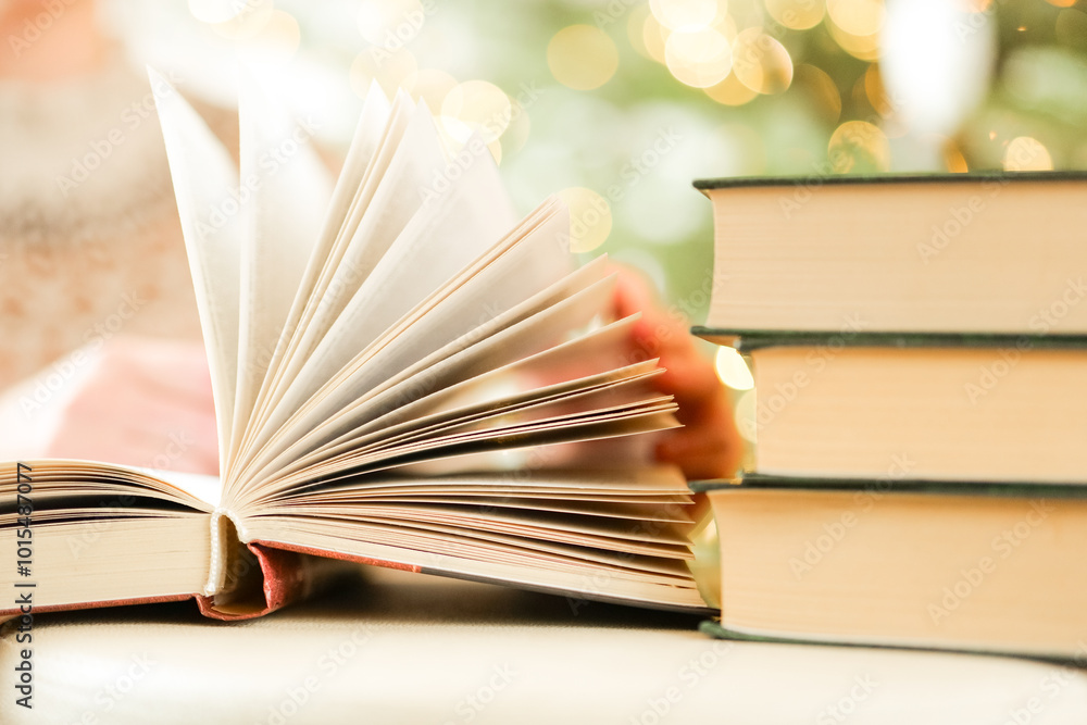 Sticker open book on a bokeh garlands background.hand turns the pages of the book.Books on winter themes. Christmas books.open book in bright room on Christmas tree background.Strong blur.Soft focus.