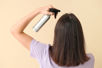 Naklejka premium Young woman with dandruff problem applying hair spray on beige background, back view