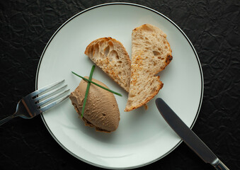 Chicken liver pate is served on a white plate with toasted bread and chives. The plate sits on a...