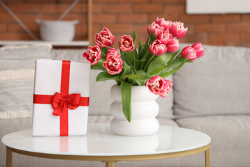 Vase with flowers and gift box on coffee table in living room
