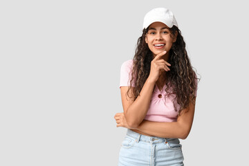 Stylish African-American woman wearing top, jeans and cap on light background