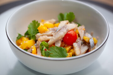 Close-up of a bowl of fish ceviche with mango chunks, cherry tomato, and fresh cilantro leaves, served in a white dish. The vibrant colors of the ingredients contrast beautifully for a fresh