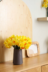 Vases with yellow narcissus flowers on shelf and chest of drawers in white room