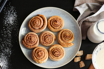 Plate with tasty baked cinnamon rolls on table in kitchen