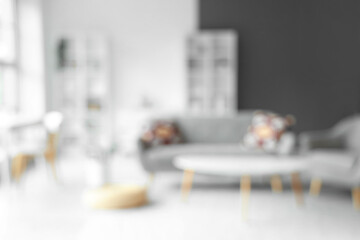 Blurred view of living room with grey sofa, tables and shelf units