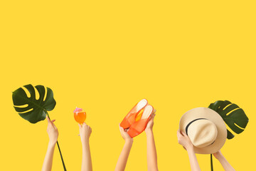 Female hands with shoes, hat, cocktail and monstera leaf on yellow background. Travel concept