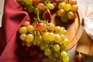 Wooden board with sweet ripe grapes and fig on white background, closeup