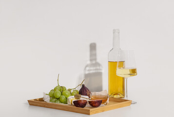 Wooden board with sweet ripe grapes, figs, camembert cheese, honey and bottle of wine on white background