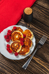 Cottage cheese pancakes with fresh raspberries on a white plate on the table