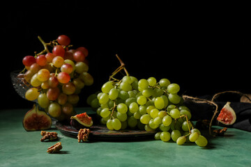 Plate with sweet ripe grapes, fig and walnuts on green background