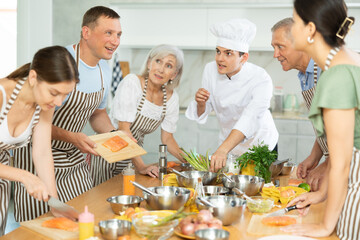 Smiling middle-aged man attendee of cooking course demonstrating piece of salmon on cutting board...