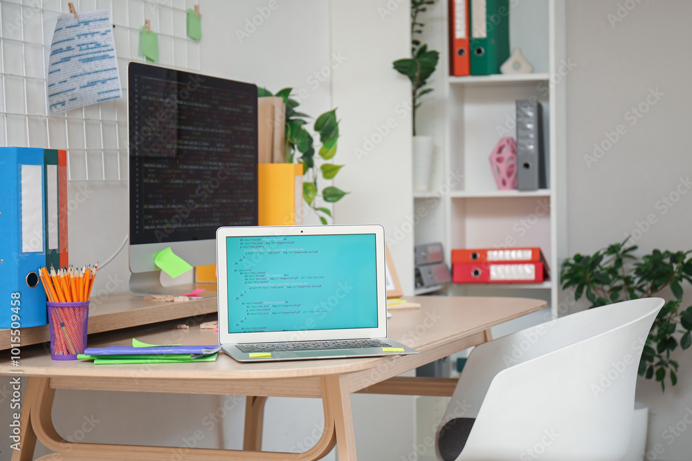 Poster laptop with code on programmer's desk in light office, closeup
