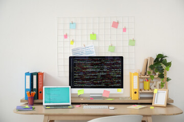 Computer monitor and laptop with codes on programmer's desk in light office