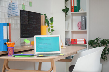 Laptop with code on programmer's desk in light office, closeup