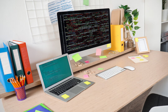 Computer monitor and laptop with codes on programmer's desk in light office