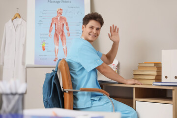 Male medical intern waving hand at table in clinic