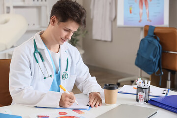 Male medical intern writing at table in clinic