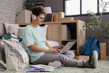 Male medical intern with headphones and laptop studying in bedroom