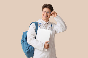 Male medical intern with backpack and laptop on beige background