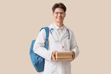 Male medical intern with backpack and books on beige background