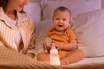 Mother with bottle of milk and her little baby in bedroom at night, closeup