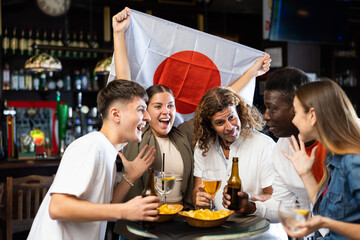 Diverse men and women supporting Japan sports team in pub together. Happy group of friends raising...
