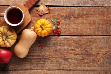 Fresh pumpkins with apple, rose hip berries and cup of tea on wooden background