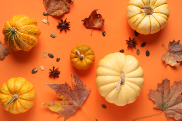 Fresh pumpkins with star anise, seeds and autumn leaves on orange background